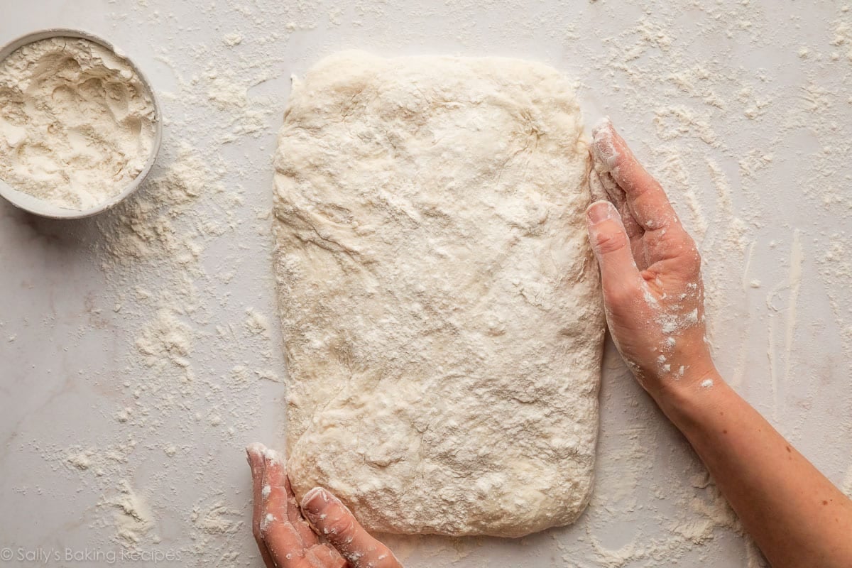 floured hands shaping dough into a flat rectangle.