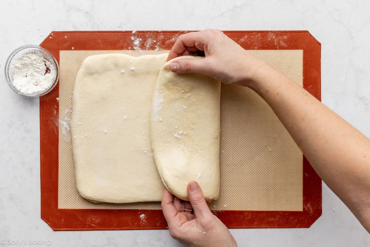 hands folding dough over itself on top of silicone baking mat.