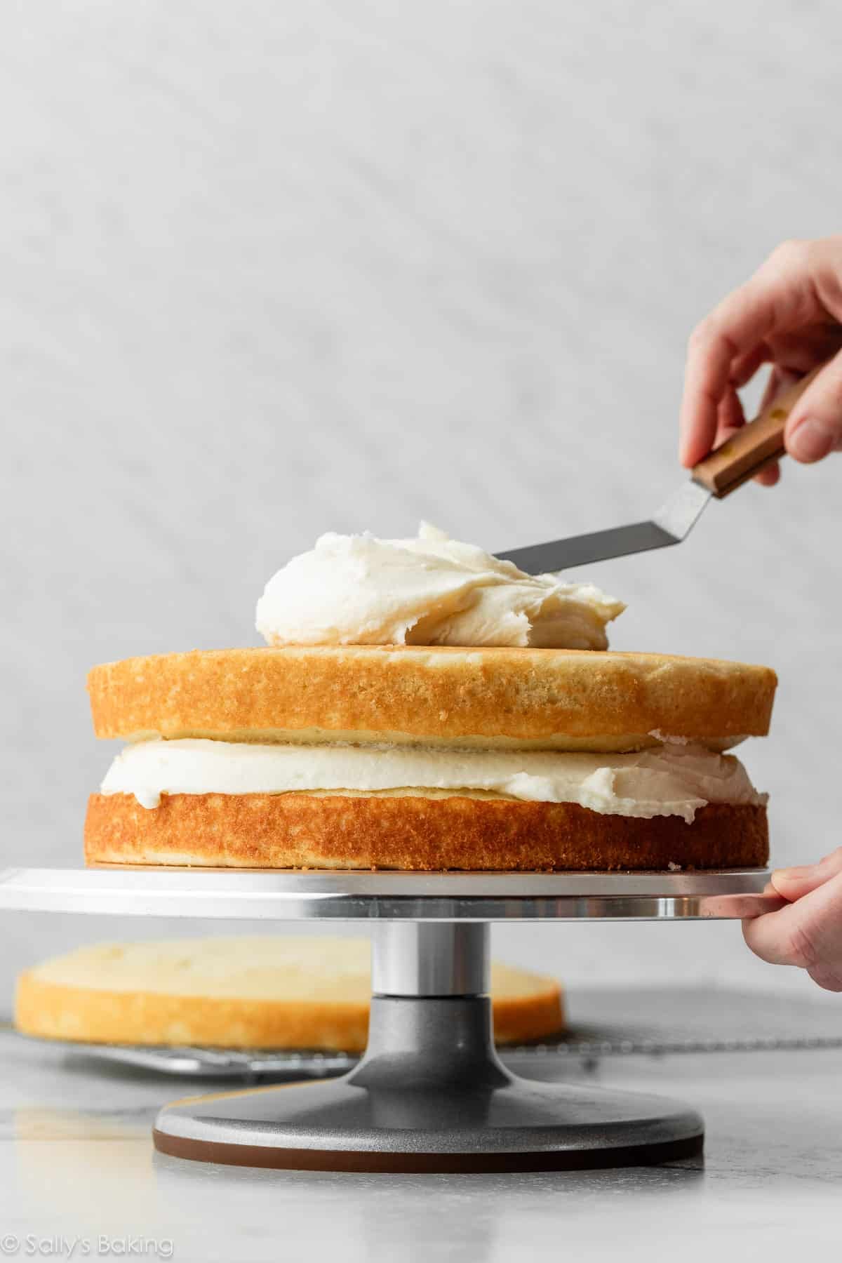 hand spreading frosting on a 2 layer cake.