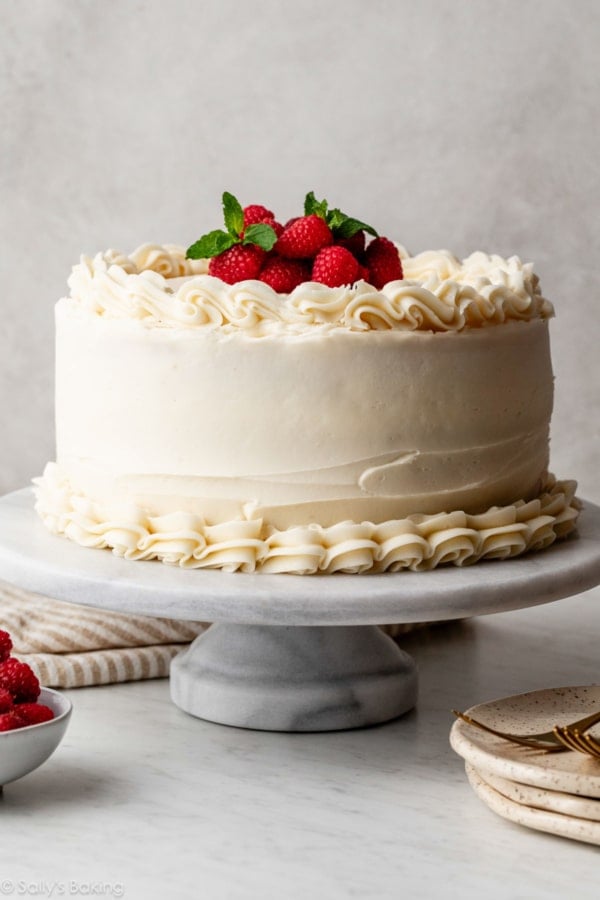 vanilla layered cake with piped vanilla frosting and fresh raspberries and mint on top.