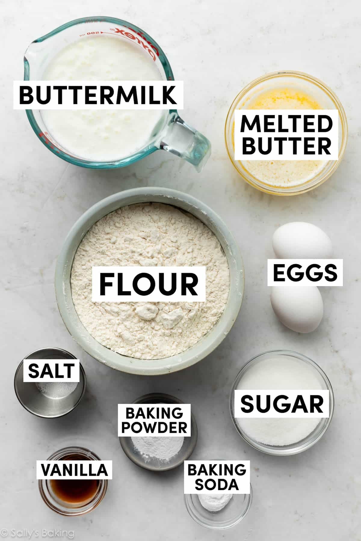 ingredients on marble surface including melted butter, flour, sugar, eggs, and vanilla.