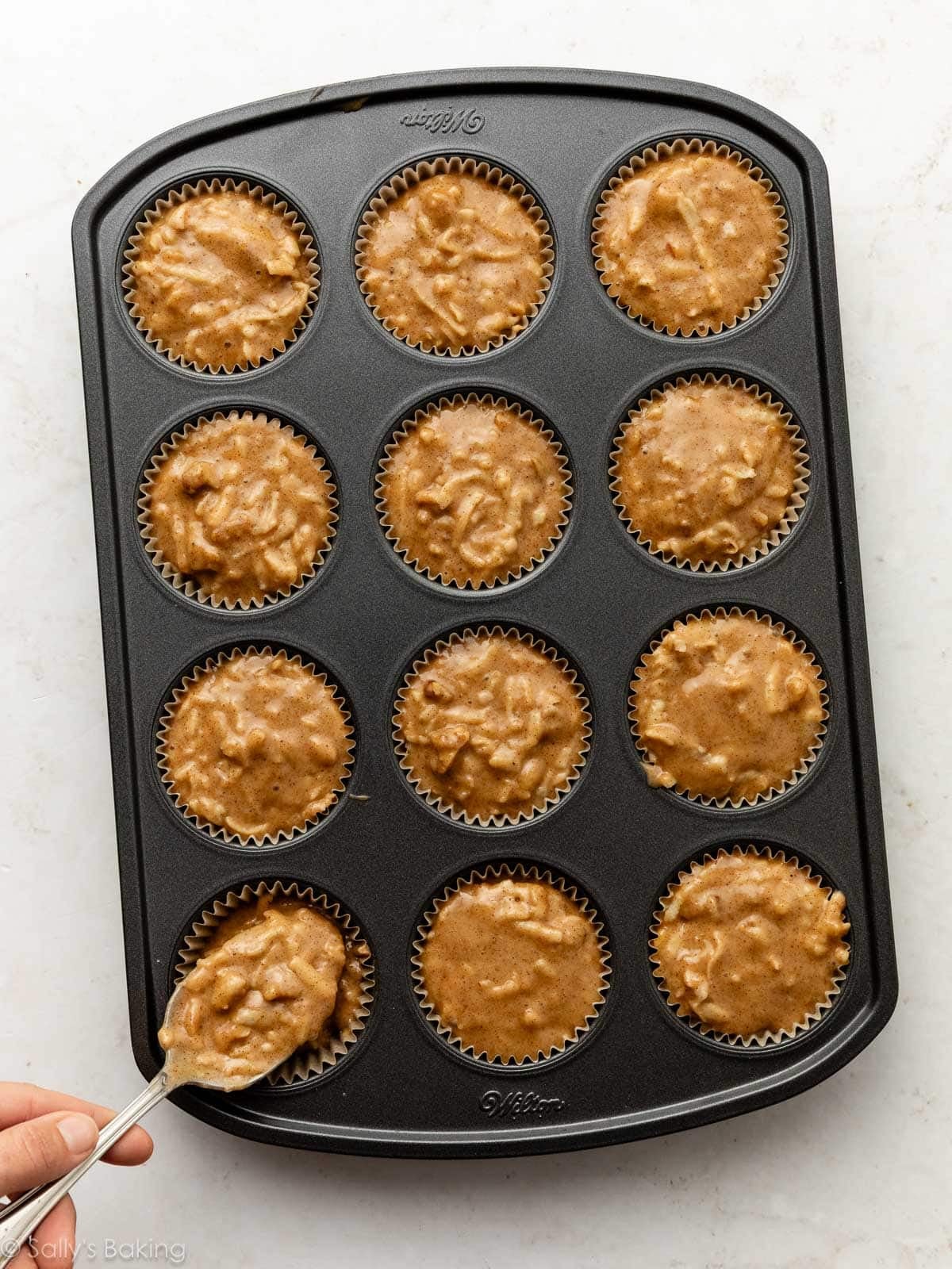 spooning apple muffin batter into muffin pan.