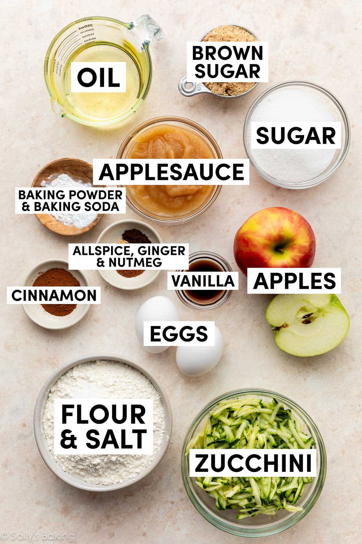 ingredients on beige surface including sugar, applesauce, flour, salt, eggs, oil, brown sugar, and spices.