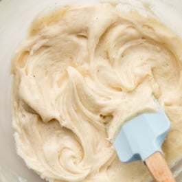 browned butter cream cheese frosting in bowl with blue spatula.