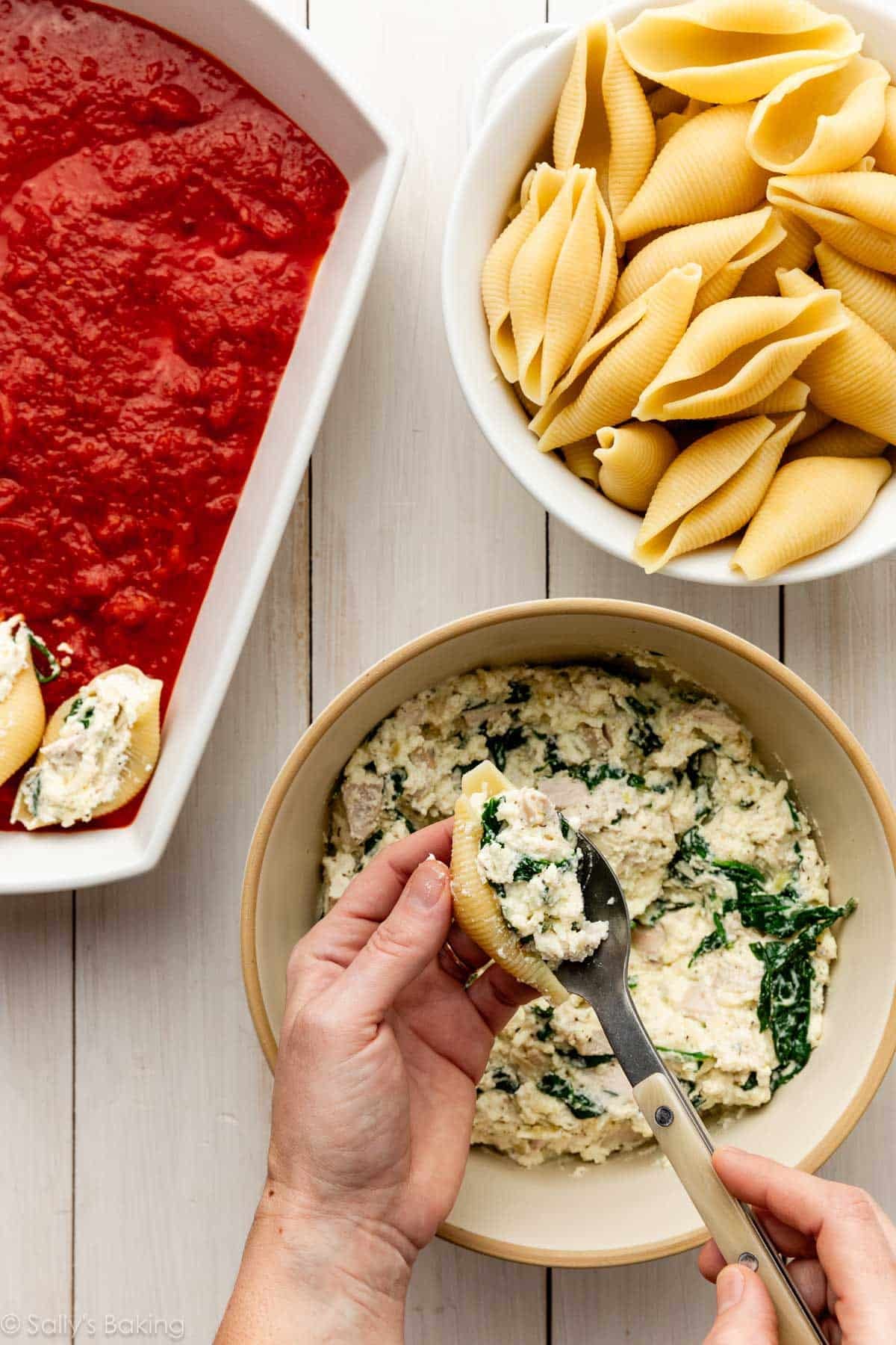 hands stuffing shells with cheesy spinach filling.